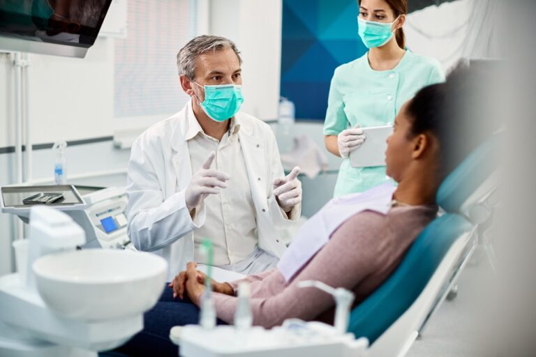 Male dentist wearing face mask while communicating with African American woman during dental appointment at dentist's office. Rising Occupancy Costs in Medical Real Estate